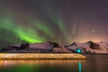 Polar Lights over mountain ridge and rocks. Ersfjord Beach. Senja, Norway