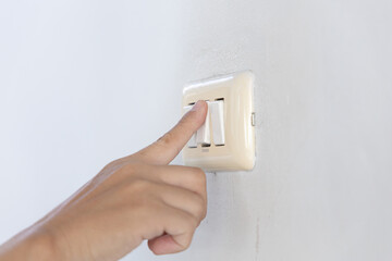 Close up young man's hand pressed the button to turn on the light switch, Open the electrical circuit beside the wall.
