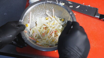 Male hands of cook in gloves stirring ingredients in iron bowl using a spoon. Arms of chef mixing...