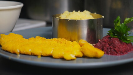 Close up male hand of cook putting mashed potatoes with the spoon into the iron mold at kitchen. Chef is serving puree with breaded chicken fillet on plate. Concept of preparing food. Slow motion