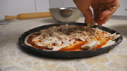Male hand putting pieces of mushrooms on pastry in metal form at cuisine. Young cook preparing tasty pizza on a wooden surface at kitchen restaurant. Concept of cooking food. Close up Slow motion
