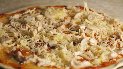 Male hands of cook putting grated cheese on pastry with ingredients in metal form at cuisine. Chef making italian pizza on a wooden surface at kitchen. Concept of cooking food. Top view Slow motion