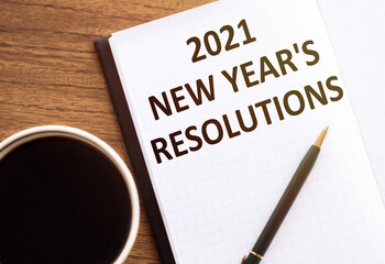 2021 NEW YEAR'S RESOLUTIONS text on notepad on wooden desk.