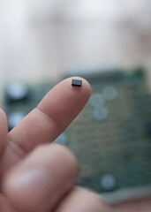 A tiny microchip on the finger of a man's hand against the background of a circuit board.The...