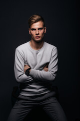 Informally ( casual ) dressed blonde young man with sharp jawline in his 20's posing in a studio in front of a black background while wearing a white sweater.