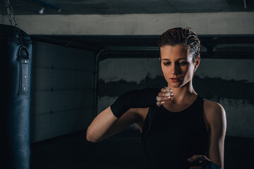 Picture of focused young woman preparing her black bandages for boxing inside a garage.