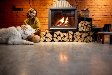 Woman sitting by the fireplace with a white dog at cozy and loft style home interior