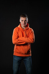 Fototapeta premium Close up portrait of a handsome male model looking serious while posing in orange hoodie inside a studio