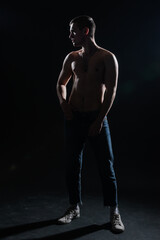 Silhouette picture of a hot shirtless muscular man posing in jeans in a dark studio.