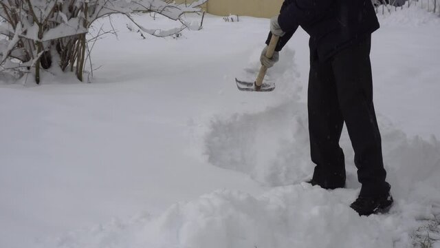 A man cleans the road from snow with a shovel, a lot of snow, winter in the village