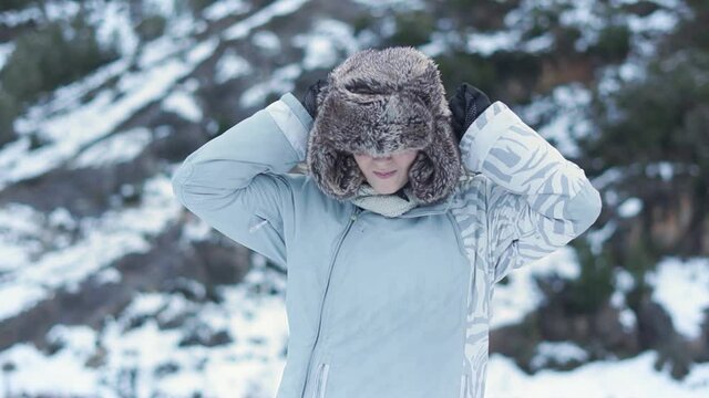 Girl putting on a winter hat in the snow.