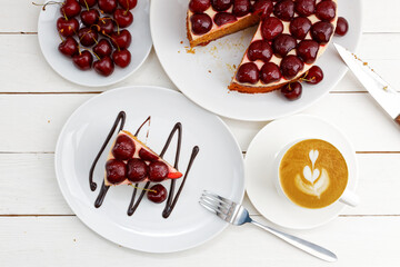 Closeup homemade cake with cherries and cup of coffee cappuccino on white wooden table. Top view.