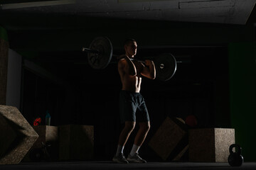  Silhouette of a fit strong shirtless athlete doing squats. Weight lifting workout concept.