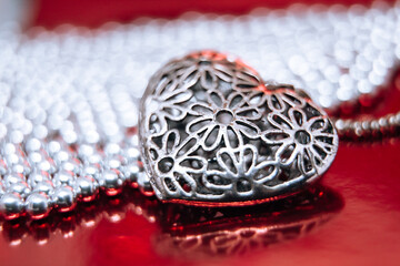 metal jewel heart with white beads , lying on red mirror background as a symbol of st Valentine Day