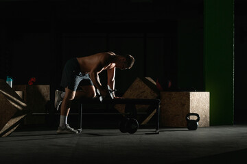 Fototapeta na wymiar Athletic caucasian man doing a dumbbell triceps kickback with his right arm on a horizontal bench.