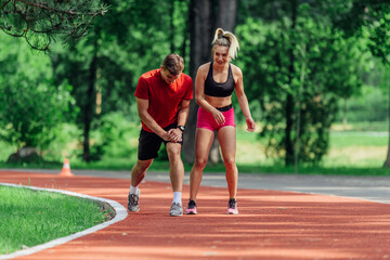 Young couple stretching before starting their morning jogging routine on a tartan track at the park.