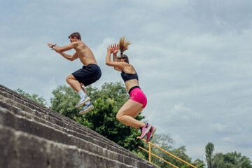 Below view of young male and female athletes jumping upstairs on the outdoor staircase .