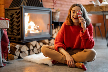 Portrait of a young happy woman with a Christmas candy by the fireplace during winter holidays