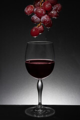 Copa de cristal con uvas goteando vino en ella. Goteo de vino en copa de cristal sobre fondo y base negra. Iluminación posterior y superior con spot.