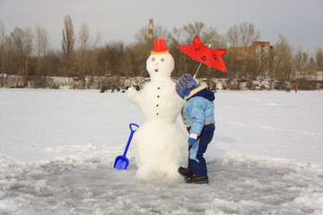 little boy in winter clothes making a snowman
