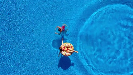 Aerial view of man dives into the the pool while girl is lying on a donut pool float