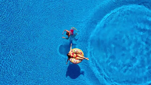 Aerial view of man dives into the the pool while girl is lying on a donut pool float