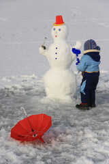 little boy in winter clothes making a snowman