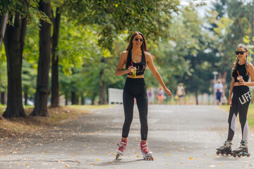Hot athletic woman in sportswear rollerblading at the park in sunny weather..
