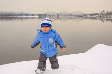 Fototapeta na wymiar portrait of a happy little boy in winter clothes against the background of a river