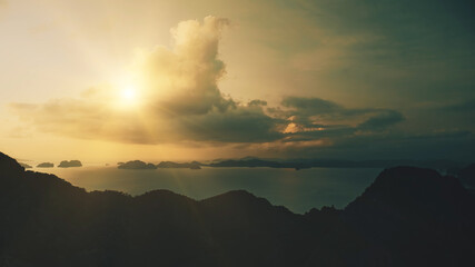 Aerial mountain island silhouette at sun shine on cloudy sky. Mounts ranges in dark tones at sun light. Epic seascape against from highlands with tropical isles. Cinematic soft shot