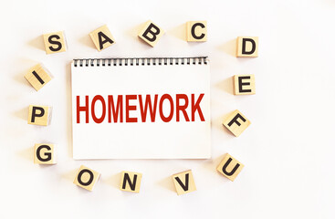 Text HOMEWORK, on notepad and white background, around are wooden cubes with letters