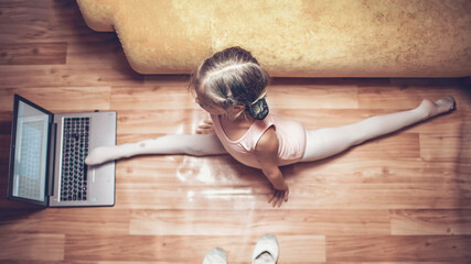 Online hobby, fitness, distant training. Young ballerina practicing classic choreography and doing leg split during online ballet class at home before laptop, social distance, online education © Maria