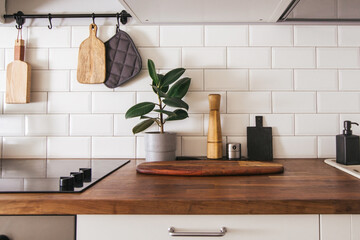 Kitchen brass utensils, chef accessories. Hanging kitchen with white tiles wall and wood tabletop.Green plant on kitchen background