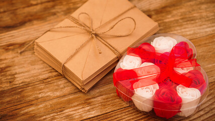Letters in craft paper envelopes and a gift of roses on a wooden background