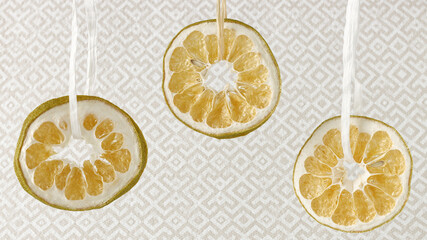 Dried grapefruit citrus slices hanging on natural rope against patterned background.