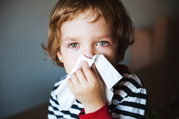 Cute little boy blowing his nose into a handkerchief.