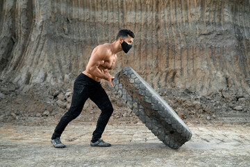 Muscular man in face mask workout with heavy wheel