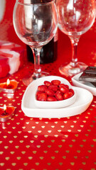 Valentines day. Bottle of vine, glasses, red roses, candles - red background. Love dinner concept - Vertical photo