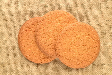 Three sweet round American cookies, close-up, on a jute fabric.