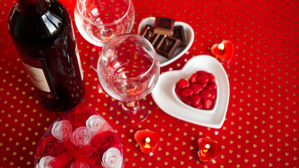 Valentines day. Bottle of vine, glasses, red roses, candles - red background. Love dinner concept