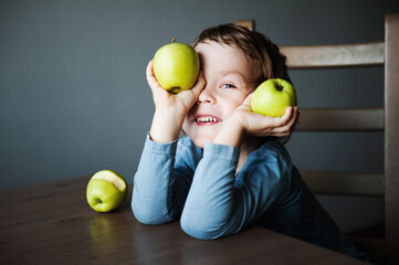 Cute preschooler boy playing with green apples. The concept of children and fruit.