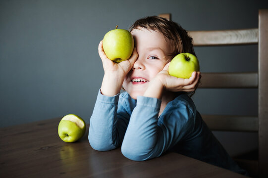 Cute preschooler boy playing with green apples. The concept of children and fruit.