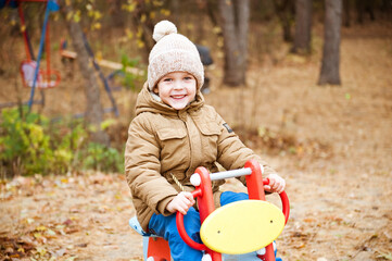 A cute preschooler boy in a knitted hat is playing in the Playground on an autumn day.