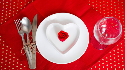 Romantic decoration of holiday table. White plates in the shape of a heart with a red rose. Red background. Top view