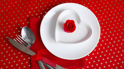 Romantic decoration of holiday table. White plates in the shape of a heart with a red rose. Red background