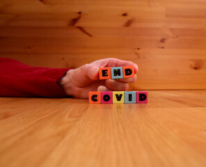 END COVID written in torn multicolored plastic cubes. Held by a hand. Close up and isolated against...