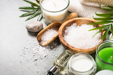 Spa product composition with cosmetics, sea salt, towel and palm leaves at stone table.