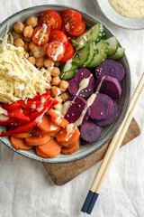 budha bowl with purple batata, bell peppers, cabbage, sweet potatoes, chickpeas, cucumbers on the white linen tablecloth
