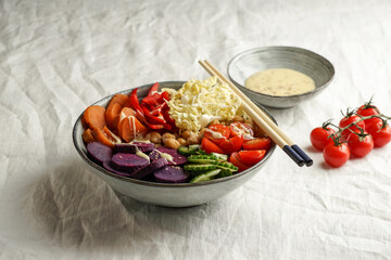 budha bowl with purple batata, bell peppers, cabbage, sweet potatoes, chickpeas, cucumbers on the white linen tablecloth