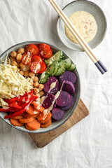 budha bowl with purple batata, bell peppers, cabbage, sweet potatoes, chickpeas, cucumbers on the white linen tablecloth